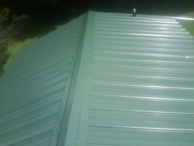 New green metal panels meeting at the ridge of a roof — Flat Roof Repair work by our crew in Germantown